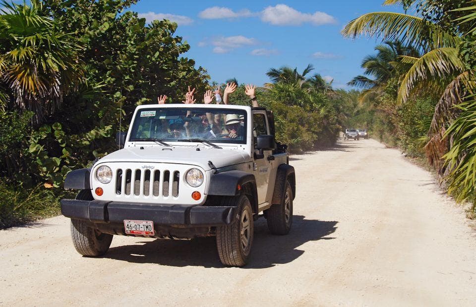 Jeep recorriendo un camino tropical entre palmeras en Quintana Roo